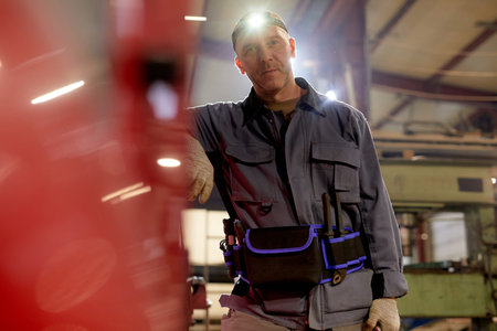 Worker in industrial environment wearing utility belt with various tools, showing signs of casual...