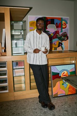 Portrait of man standing in art studio holding cup and looking at camera He is surrounded by colorful paintings and various art suppliesの写真素材