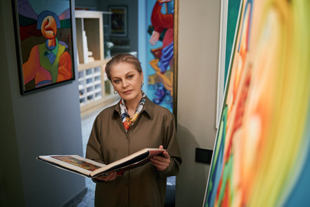 Senior Caucasian woman reading a book in an art gallery surrounded by colorful paintings and modern artworkの写真素材