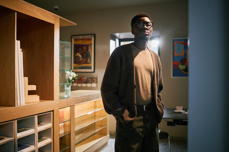 Portrait of an African American man wearing sunglasses, standing in a well-lit room with modern decor and furnitures surrounding heの写真素材