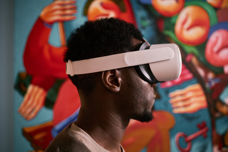 Black man using VR headset and looking at art in gallery setting with colorful abstract paintings creating vivid and immersive environmentの写真素材