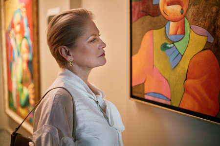 Woman admiring colorful abstract painting in museum showcasing modern art. Reflecting on artistic style and colors without external distractionsの写真素材