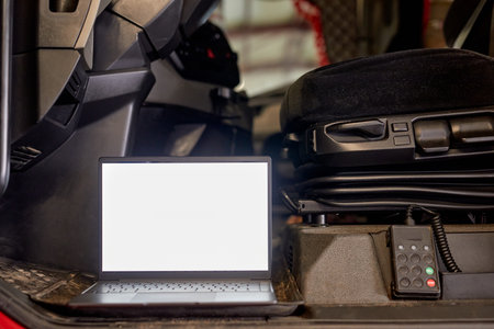 Laptop positioned on dashboard near drivers seat inside vehicle cabin. Visible controls and seat indicate equipment setup for work or monitoring purposesの写真素材