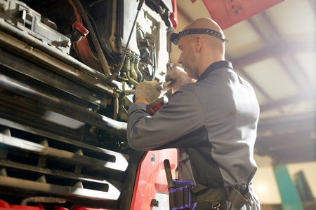 Mechanic wearing protective gear is examining and fixing an engine in a spacious, well-lit workshop setting. Patiently handling tools and machinery with focus and precisionの写真素材