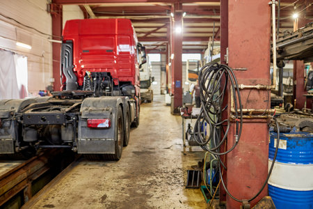Truck positioned inside maintenance workshop undergoing repair with tools, equipment, and various items scattered around highlighting industrial settingの写真素材