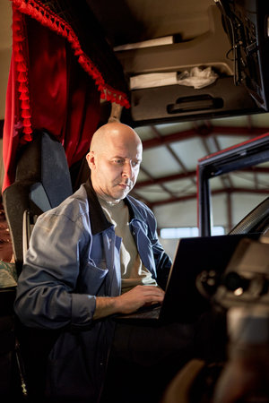 Portrait of bald man in blue jacket and gray shirt sitting inside vehicle cabin, working on something with focused expressionの写真素材