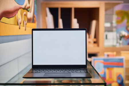 Open laptop positioned on glass table in modern art studio with colorful paintings adorning walls. Vibrant artwork creating an inspiring atmosphere for creative workの写真素材
