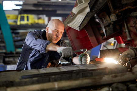 Mechanic focused on repairing vehicle engine in workshop environment, showcasing technical skill and...