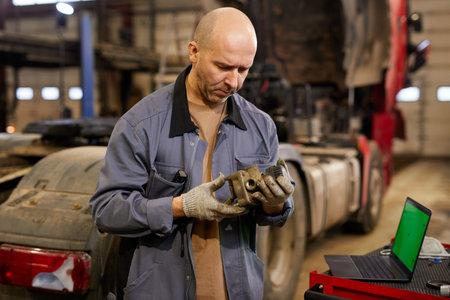 Mechanic in auto repair shop meticulously inspecting a car part with focused demeanor, dressed in work attire, with tools and devices surrounding himの写真素材