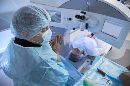 Middle aged male surgeon preparing for eye surgery on woman lying under ophthalmic laser system in modern operating room with medical instruments visibleの写真素材