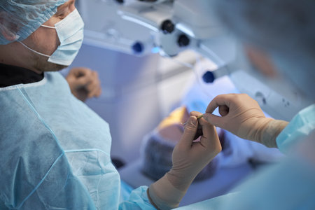 Middle aged man wearing surgical mask and gown assisting middle aged woman preparing medical instrument in operating room during surgical procedureの写真素材
