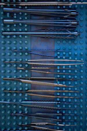 Sterile surgical instruments arranged in organized rows on blue perforated tray, showing various...