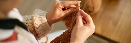 Detailed close-up image showing hands expertly knitting a cozy sweater with beige yarn, capturing intricate details of knitting process. Wooden table and soft light create warm atmosphereの写真素材
