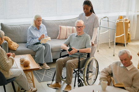 Elderly residents engaging in various activities in common room of assisted living home with nurse standing by, providing support and care. Warm, welcoming atmosphere creating comfortable environmentの写真素材
