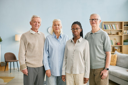 Portrait of diverse family with three seniors and one younger adult standing in modern living room. All members smile softly, exuding warmth and unity amidst homely surroundingsの写真素材