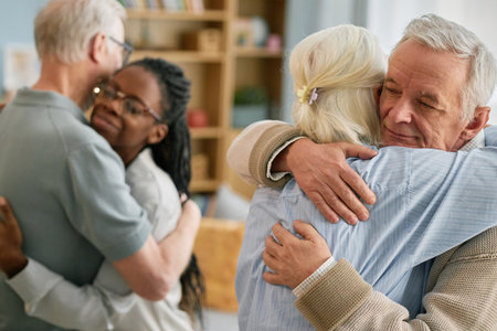 Elderly couple warmly embracing younger family members in cozy living room with soft lighting and decor creating comforting and affectionate atmosphere showcasing family bondsの写真素材