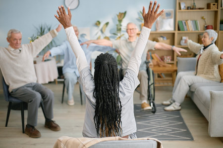 Instructor leading group exercise with senior participants seated in living room setting. Highlighting active engagement, this scene captures enthusiasm and focused commitmentの写真素材