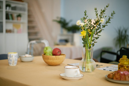 Beautifully set brunch table featuring a vase of fresh flowers, a bowl with fruits, and a coffee...