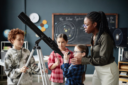Black woman teaching group of children using telescope in classroom, three kids including boy and...