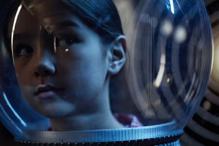 Portrait of Asian child looking to side wearing transparent astronaut helmet, face partially...