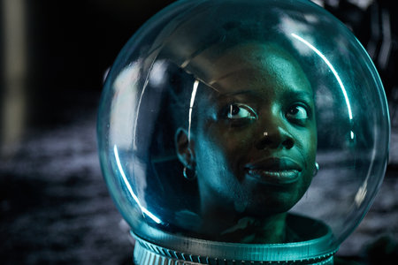 Portrait of young adult Black woman gazing upward inside transparent astronaut helmet, face...