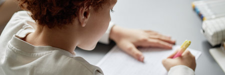 Website header shot of Caucasian child writing with yellow pen on lined paper at desk, showing...