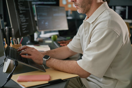Caucasian middle aged man working on laptop at desk in office, typing on keyboard with smartwatch on...