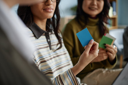 Multiethnic group of teenage girls participating in counseling session holding colored cards,...
