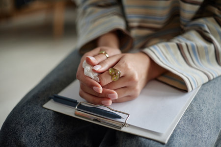 Teenager girl sitting during counseling session holding tissue in hands resting on clipboard with...