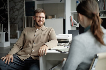 Caucasian young adult man smiling and talking with Caucasian young adult woman in modern office...
