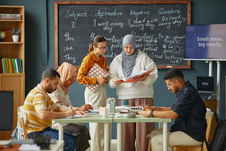 Diverse group of young adult men and women collaborating on language exercises in classroom,...