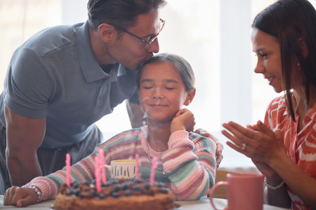 Caucasian man kissing head of smiling child girl with closed eyes while sitting at table with...