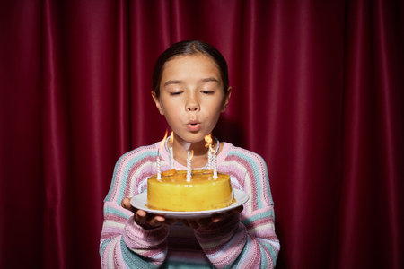 Portrait of preteen Caucasian girl blowing out candles on birthday cake while standing in front of...