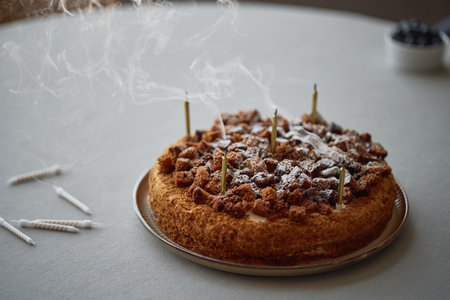 Birthday cake with extinguished candles emitting smoke sitting on table, scattered unlit candles...