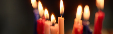 Header of colorful Hanukkah candles burning on menorah, flames glowing against dark background, wax melting down sides, traditional Jewish holiday celebration symbolizing Festival of Lightsの写真素材
