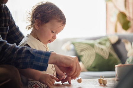 Caucasian child playing with wooden dreidels beside adult man during Hanukkah, both focusing on...