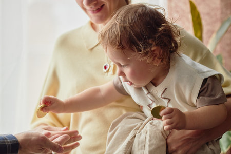 Caucasian woman holding toddler child handing chocolate coins to outstretched hand during Hanukkah...
