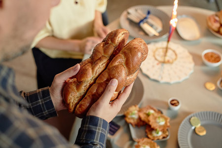 Caucasian middle aged man holding braided challah bread with both hands near Hanukkah table while...