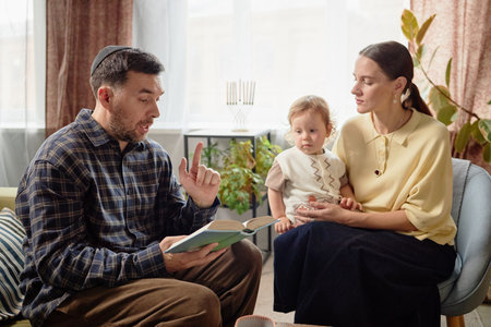Caucasian middle aged man reading book aloud while gesturing, sitting beside young woman holding...