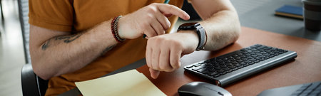 Header of man sitting at desk checking smartwatch while holding pen near computer keyboard and...