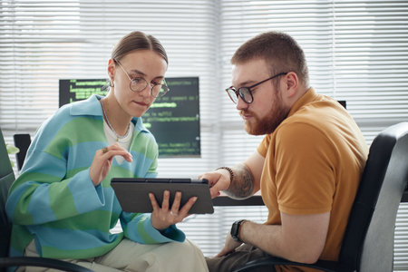 Young adult Caucasian woman and man sitting together using digital tablet, collaborating on project...