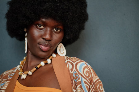 Portrait of young adult Black woman looking into camera wearing large earrings and beaded necklace...