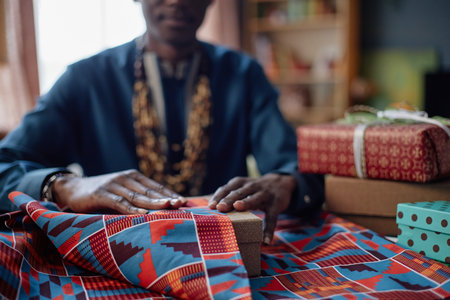 Black man wrapping gift box with vibrant patterned fabric, hands carefully folding edges,...