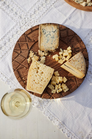 Assorted cheese blocks and cubes arranged on wooden board with glass of wine nearby, showing close...
