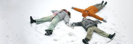 Header of family of parents and kid lying on snow creating snow angels, arms and legs spread wide,...