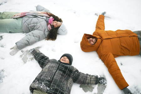 Caucasian man, woman and child lying on snow making snow angels, smiling and looking up, winter outdoor activity, family enjoying time togetherの写真素材