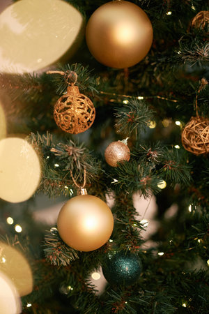Closeup showing decorated Christmas tree with gold and green ornaments hanging among pine branches,...