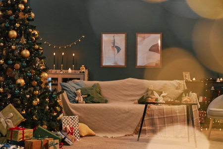 Living room decorated for Christmas featuring large Christmas tree with ornaments and wrapped gifts, sofa with cushions and blankets, candles and festive decorations on shelvesの写真素材
