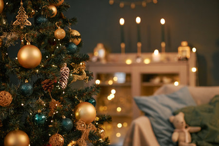 Christmas tree decorated with gold and blue ornaments standing in living room, glowing candles and string lights illuminating background, plush bear sitting on sofa nearbyの写真素材