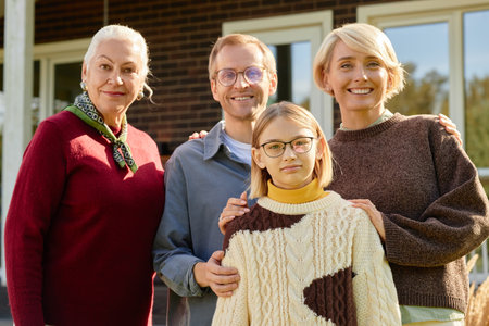 Senior woman, middle aged man and woman, teen girl standing together outdoors smiling at camera in...